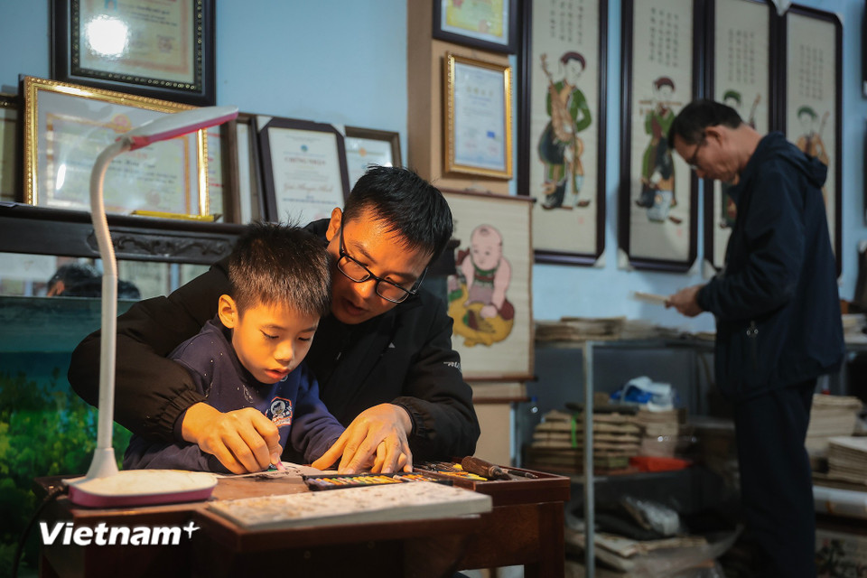 Ngoài giờ học trên lớp, Minh rất hứng thú với những bức tranh mà bố với ông nội làm, tò mò và lắng nghe về câu chuyện mà tranh Đông Hồ kể, bắt đầu làm quen từ việc tô màu. (Ảnh: Hoài Nam/Vietnam+)
