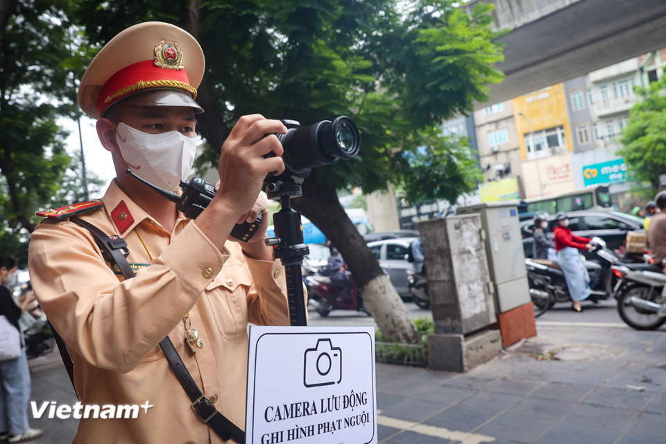 Máy được đặt lên chân máy, phía trước có tấm bảng "Camera lưu động ghi hình phạt nguội" để thông báo cho người đi đường biết. (Ảnh: Hoài Nam/Vietnam+)