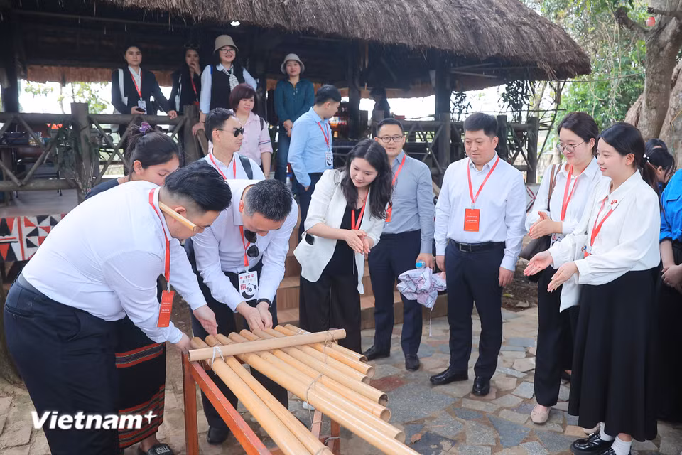 Thanh niên Trung Quốc trải nghiệm sử dụng đàn K'lông pút. Người chơi đàn để hai bàn tay gần đầu ống nứa rồi vỗ tay vào nhau khiến hơi tác động vào cột không khí của ống phát ra âm thanh. (Ảnh: Hoài Nam/Vietnam+)