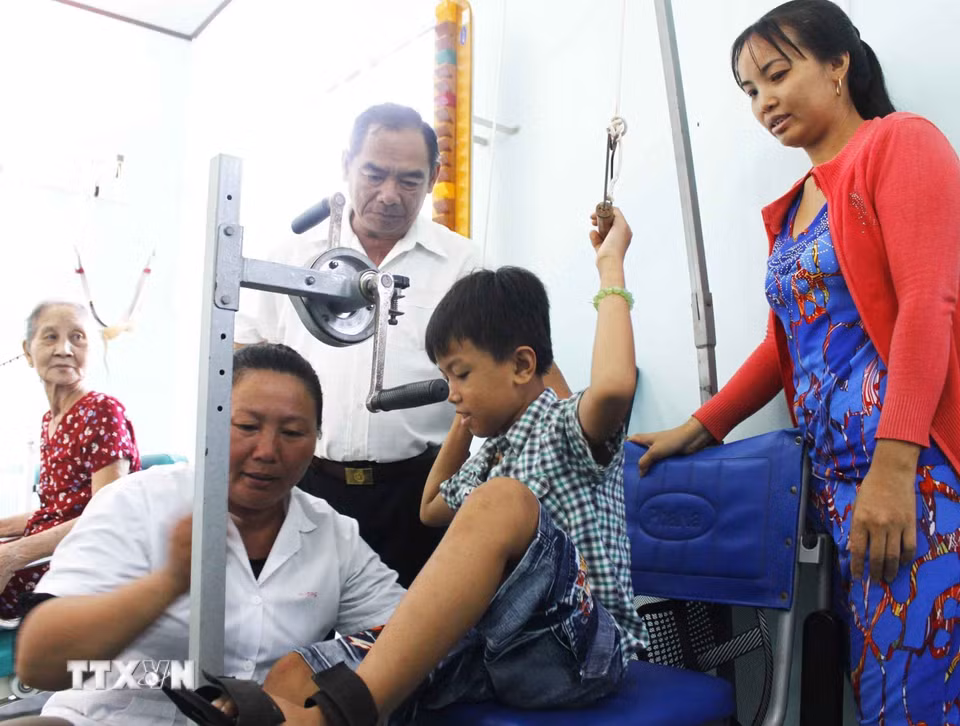 Ngày 22/4/2017, Hội nạn nhân chất độc da cam/dioxin tỉnh Vĩnh Long phối hợp với nhà tài trợ trao tặng bộ dụng cụ tập luyện cho Trung tâm phục hồi chức năng nạn nhân chất độc da cam/dioxin huyện Tam Bình, tỉnh Vĩnh Long. Với tổng giá trị trên 40 triệu đồng. Trong ảnh: Đại diện nhà tài trợ thăm và hướng dẫn trẻ luyện tập phục hồi chức năng. (Ảnh: Lê Thúy Hằng/TTXVN)