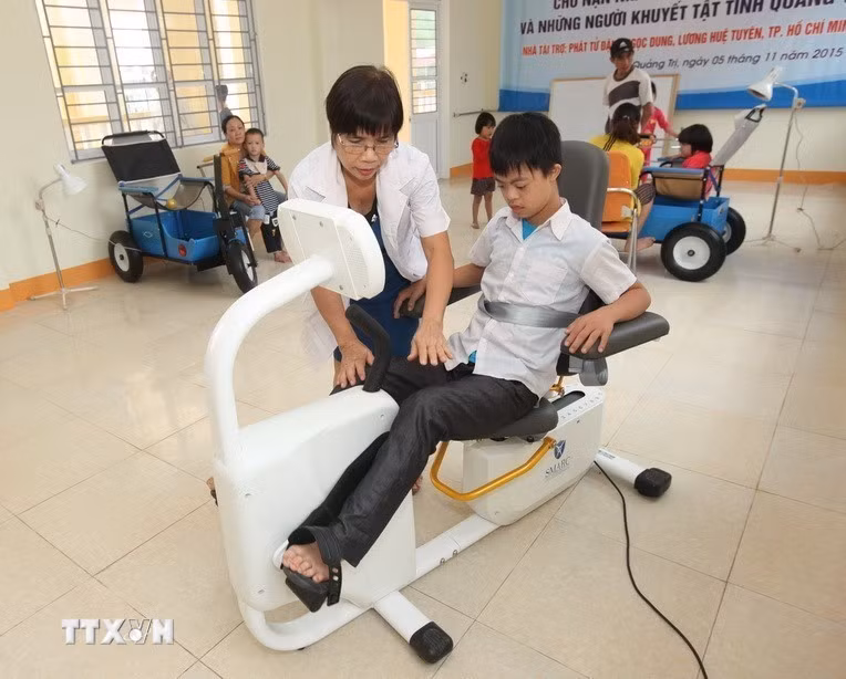 Nhân viên Trung tâm Nuôi dưỡng, phục hồi chức năng và dạy nghề cho nạn nhân chất độc da cam tại thành phố Đông Hà, tỉnh Quảng Trị giúp trẻ em là nạn nhân chất độc da cam/dioxin tập phục hồi chức năng (2015). (Ảnh: Anh Tuấn/TTXVN)