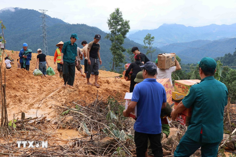 Hàng hóa được chuyển đến điểm đầu sạt lở, sau đó các lực lượng vận chuyển chuyền tay nhau, mỗi người vận chuyển một đoạn, rồi tiếp tục chuyển cho người khác, để vượt qua hơn 200 mét đường bị bùn đất do sạt lở núi vùi lấp. (Ảnh: Đoàn Hữu Trung/TTXVN)