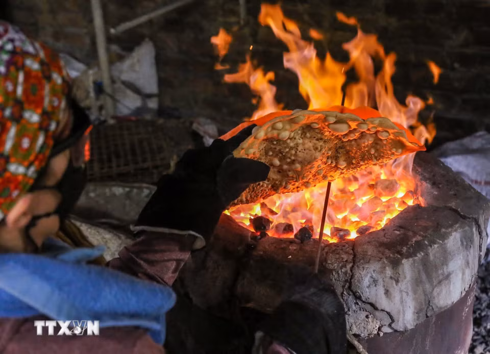 Để có những chiếc bánh đa dừa nướng thơm ngon, người thợ làng Thổ Hà phải ngồi bên bếp than hồng rực lửa hàng giờ đồng hồ, nhanh tay xoay đều để bánh chín vàng ruộm, giòn tan mà không bị cháy. (Ảnh: Hà Anh/TTXVN phát)