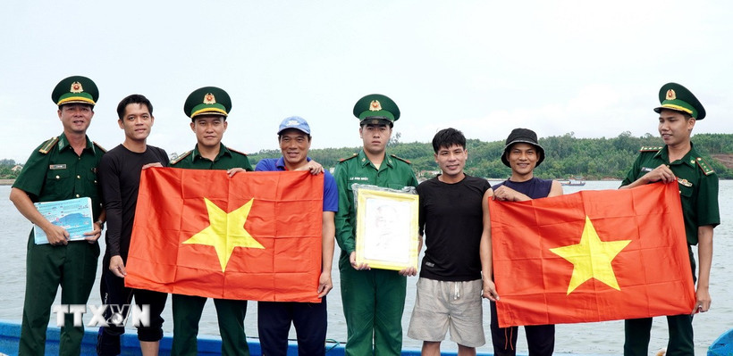 Lực lượng Biên phòng tặng cờ Tổ quốc và ảnh Bác Hồ cho ngư dân tham gia khai thác hải sản xa bờ. (Ảnh: Lê Phước Ngọc/TTXVN)