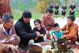 Các cháu nhỏ được thầy mo (thầy cúng) và các già làng, trưởng bản, người có uy tín buộc chỉ vào cổ tay và nhập họ, chính thức đặt tên sau khi lễ cúng làm vía cho bản làng kết thúc. (Ảnh: Xuân Tiến/TTXVN)