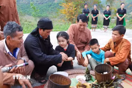 Các cháu nhỏ được thầy mo (thầy cúng) và các già làng, trưởng bản, người có uy tín buộc chỉ vào cổ tay và nhập họ, chính thức đặt tên sau khi lễ cúng làm vía cho bản làng kết thúc. (Ảnh: Xuân Tiến/TTXVN)