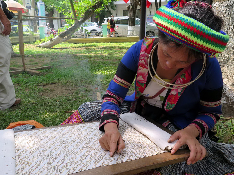 Thợ thủ công vẽ sáp lên nền vải để tạo hoa văn trước khi cho vào nhuộm. (Ảnh: Quốc Việt/TTXVN)