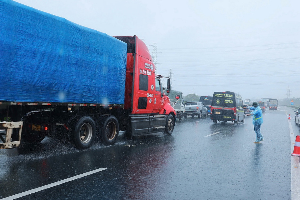 Nhân viên Công ty BOT Pháp Vân-Cầu Giẽ hướng dẫn các phương tiện đi sang bên trái, tránh vùng ngập sâu bên phải tại đoạn Km191+500 trên cao tốc Pháp Vân-Cầu Giẽ (ảnh chụp lúc 10h25 ngày 11/9). (Ảnh: Hoàng Hiếu/TTXVN)