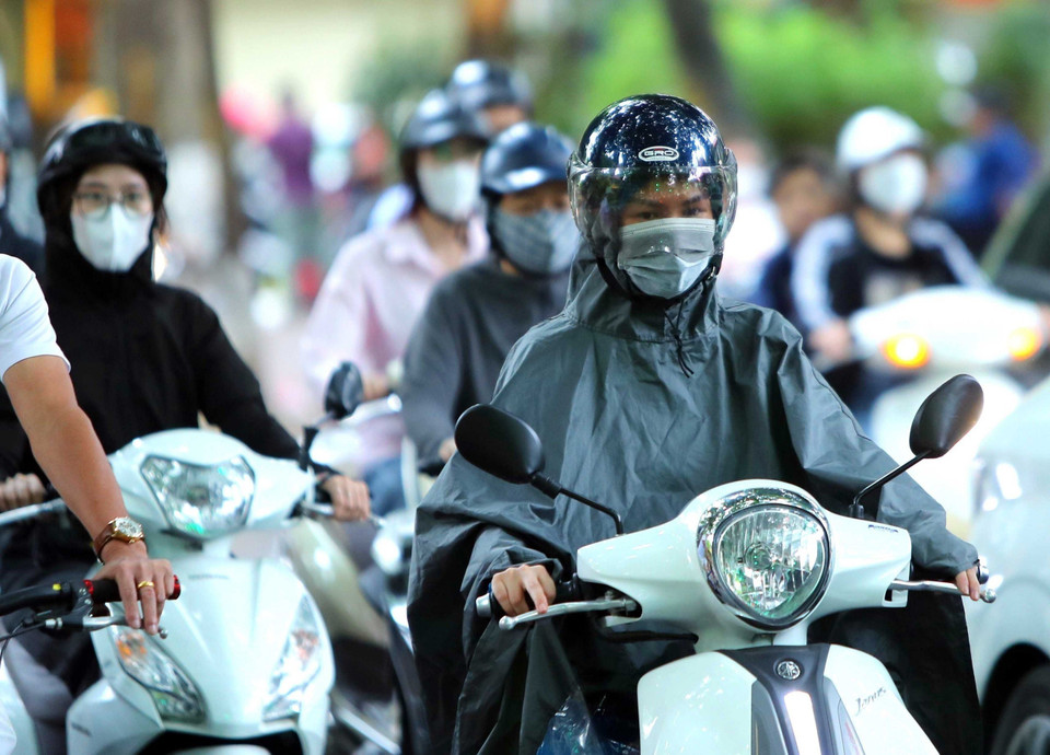 Mưa lạnh khiến nhiều người phải mặc thêm áo mưa khi ra đường. (Ảnh: An Đăng/TTXVN)