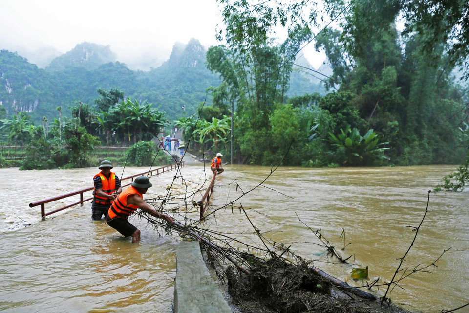 Lực lượng chức năng xã Mai Sao, huyện Chi Lăng vớt rác trôi, mắc vào lan can cầu dân sinh đi vào thôn Nà Lốc. (Ảnh: Phạm Hậu/TTXVN)
