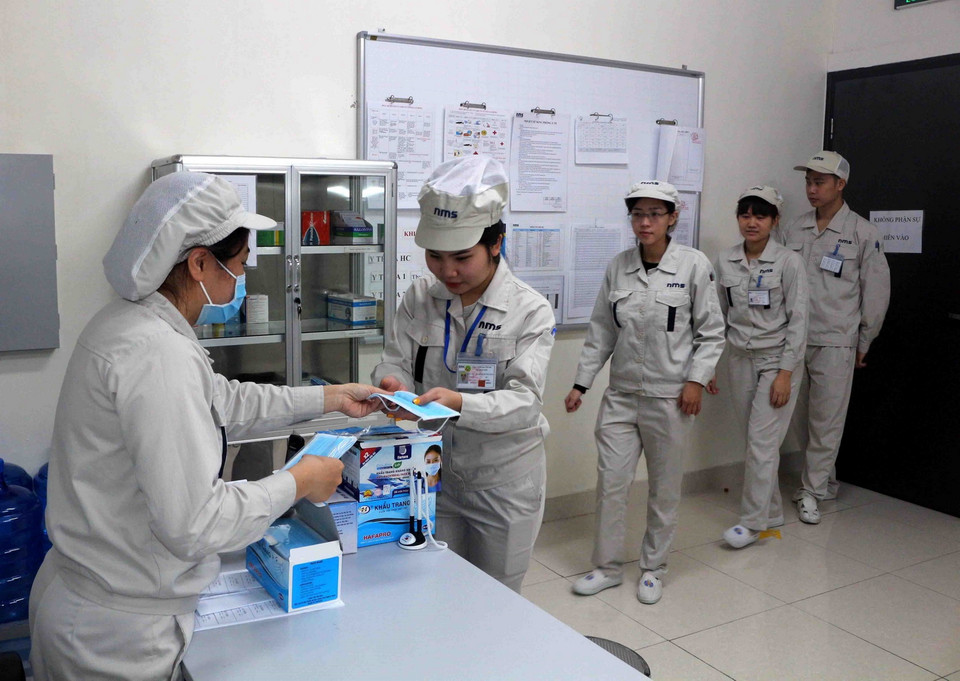 Công nhân Công ty TNHH NMS Việt Nam (Hà Nam) được phát mỗi ngày 1 chiếc khẩu trang y tế trước khi vào làm. (Ảnh: Đại Nghĩa/TTXVN)