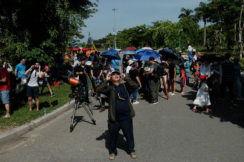 Sử dụng kính chuyên dụng để ngắm hiện thực nhật thực một phần tại công viên Hòa Bình. (Ảnh: Hoàng Việt/TTXVN)