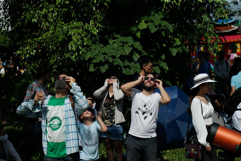 Sử dụng kính chuyên dụng để ngắm hiện thực nhật thực một phần tại công viên Hòa Bình. (Ảnh: Hoàng Việt/TTXVN)