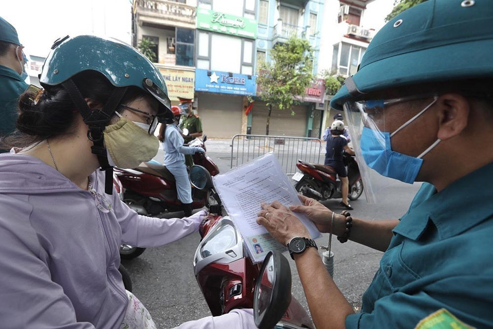 Lực lượng chức năng tại chốt kiểm soát phường Đống Mác (quận Hai Bà Trưng) nhắc nhở người dân cần hoàn thiện các mục còn thiếu đối với giấy đi đường theo quy định mới. (Ảnh: Minh Quyết/TTXVN)