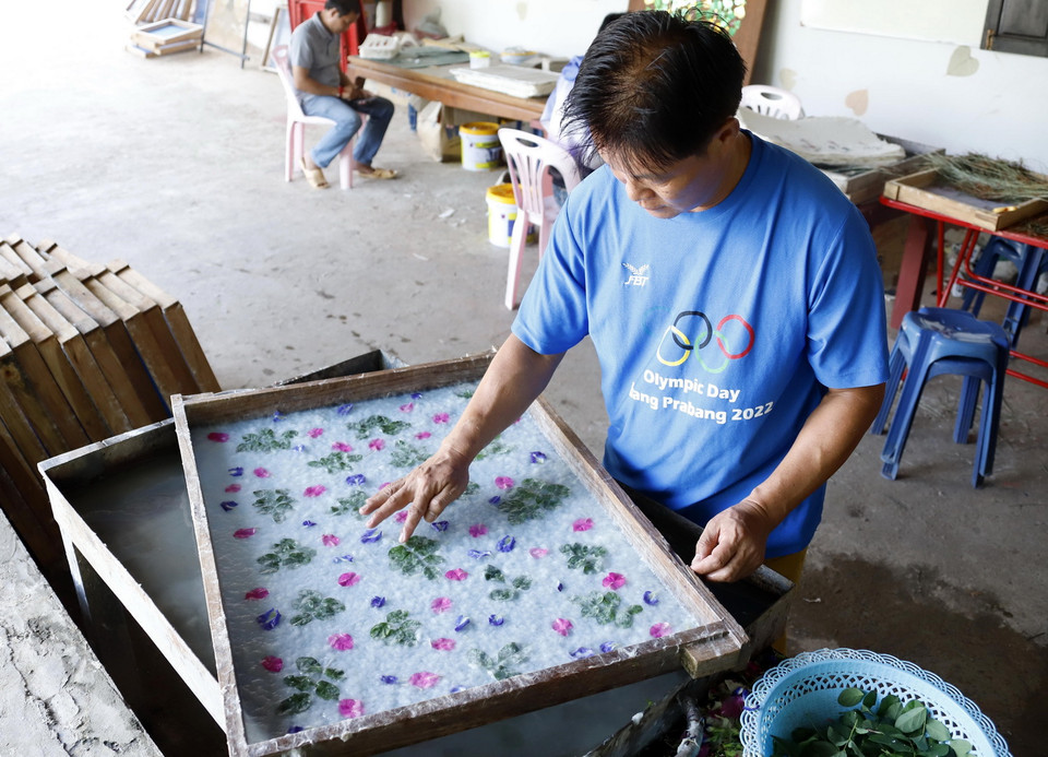 Nghệ nhân Nalongkone Khounphachansi, chủ cơ sở làm giấy Saa tại bản Xienglek, tỉnh Luang Prabang, trang trí hoa lá lên khuôn giấy. (Ảnh: Phạm Kiên/TTXVN)