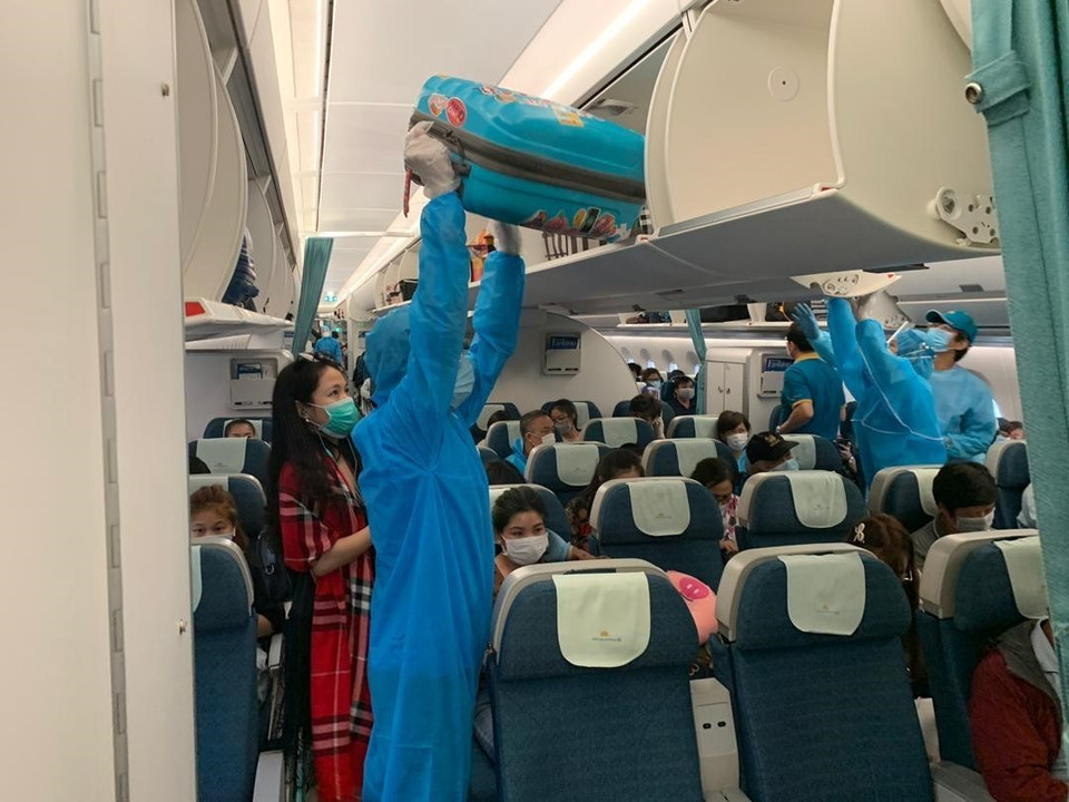 Các tiếp viên Vietnam Airlines trong bộ đồ bảo hộ y tế hỗ trợ hành khách xếp hành lý trên tàu bay, trước khi khởi hành về nước. (Ảnh: Hà Ngọc/TTXVN)
