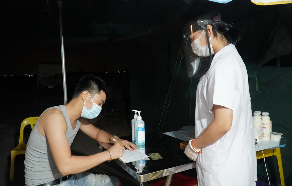 Lực lượng y tế tại chốt kiểm dịch chân cầu Yên Dũng nối tỉnh Bắc Ninh và Bắc Giang hỗ trợ người dân khai báo y tế. (Ảnh: Đinh Văn Nhiều/TTXVN)