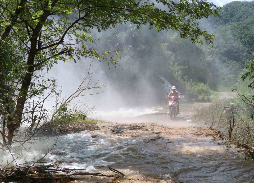 Người dân gặp khó khăn khi đi qua những điểm xuất hiện dòng thác lũ đổ xuống từ vách núi bên đường. (Ảnh: Xuân Tiến/TTXVN)