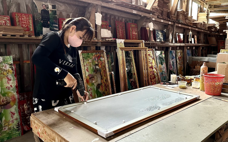 Trải qua gần trăm năm thăng trầm, làng nghề vẫn được những nghệ nhân giữ gìn và phát huy. Trong ảnh: Đóng khung tranh kính để giao hàng cho khách. (Ảnh: Thanh Sang/TTXVN)