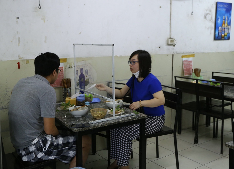 Khách tại quán ăn trên phố Đại Cồ Việt có lắp tấm chắn giọt bắn đảm bảo phòng chống COVID-19. (Ảnh: Hoàng Hiếu/TTXVN)