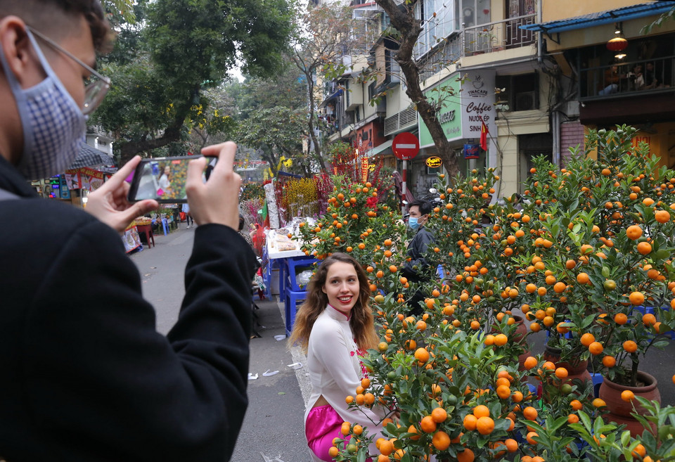 Du khách nước ngoài trong trang phục áo dài Việt Nam thích thú chụp ảnh tại chợ hoa Hàng Lược. (Ảnh: Hoàng Hiếu/TTXVN)