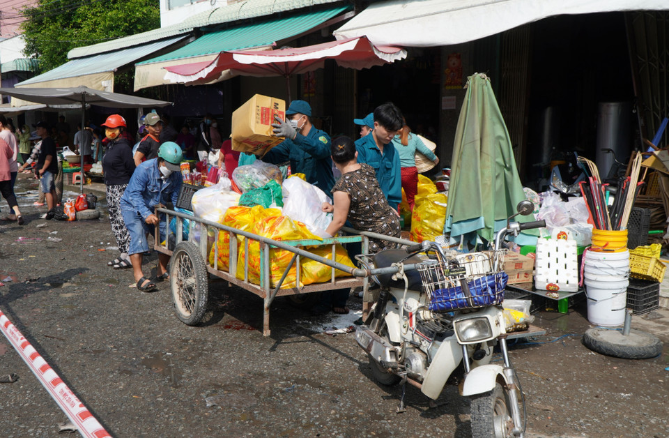 Lực lượng chức năng hỗ trợ người dân mang hàng hóa ra ngoài. (Ảnh: Nhựt An/TTXVN)