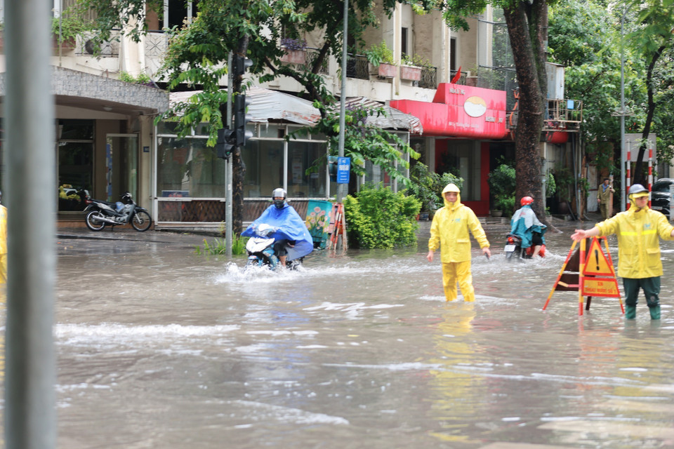 Công nhân môi trường đô thị Hà Nội hướng dẫn các phương tiện di chuyển qua đoạn ngập ở ngã tư Phan Bội Châu-Lý Thường Kiệt, quận Hoàn Kiếm. (Ảnh: Hoàng Hiếu/TTXVN)