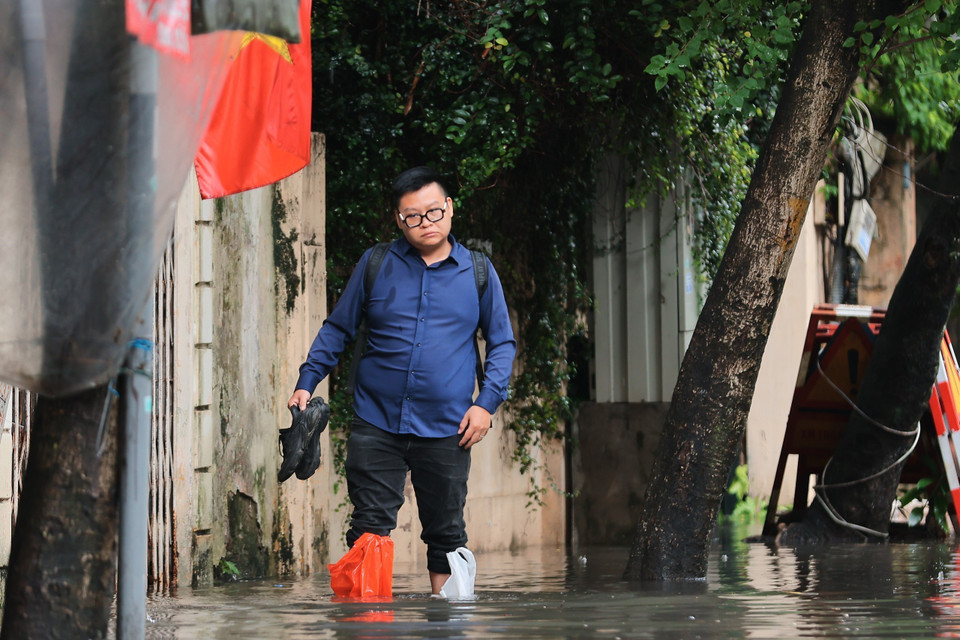 Nhiều người phải lội ra khỏi nhà để đến cơ quan vì không còn đường nào khác hay không thể chờ đến khi nước rút. (Ảnh: Hoàng Hiếu/TTXVN)