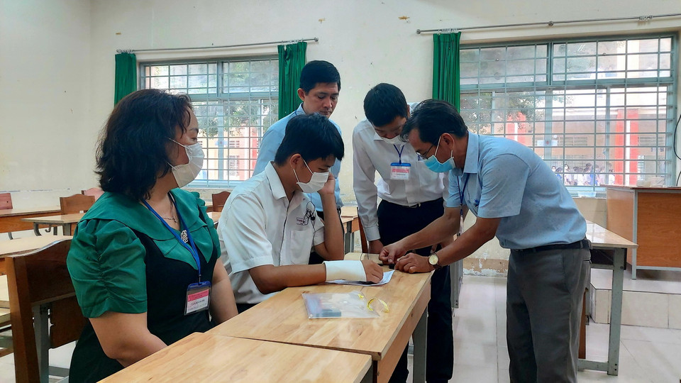  Các giám thị hỗ trợ gắn thiết bị ghi âm giám sát quá trình thi môn Ngữ Văn của thí sinh Tạ Quốc Hùng tại điểm thi Trường THPT Bùi Hữu Nghĩa, quận Bình Thủy, thành phố Cần Thơ bị tai nạn gãy tay nên không thể làm bài thi môn Ngữ Văn. (Ảnh: Hồng Thái/TTXVN)