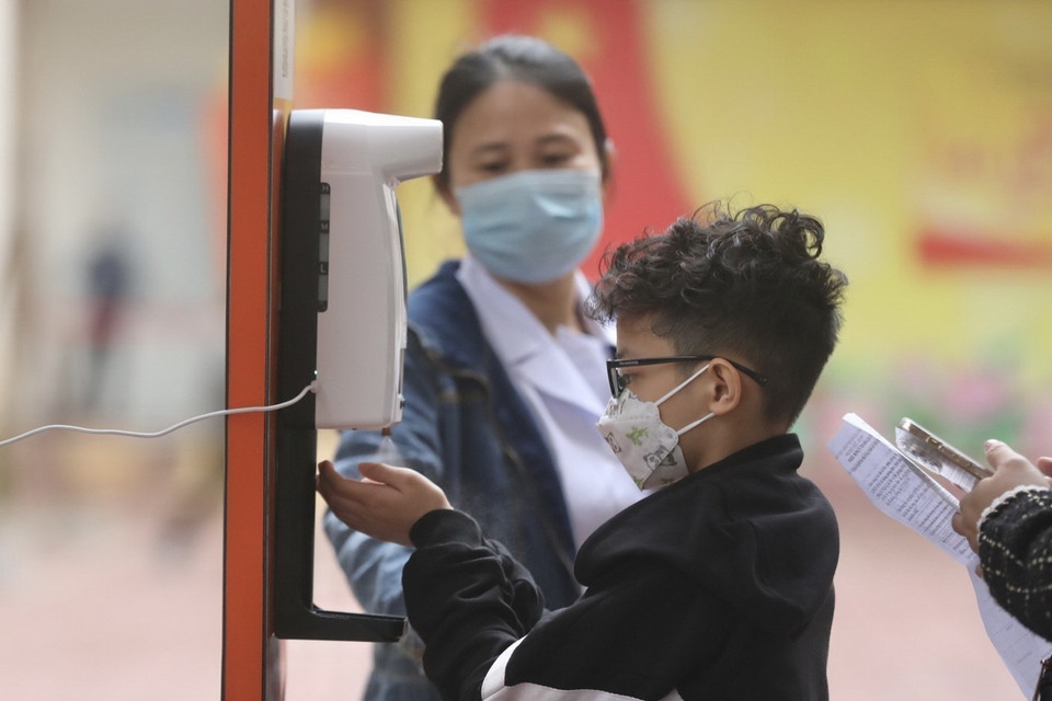 Học sinh và người nhà được hướng dẫn sát khuẩn tay và kiểm tra thân nhiệt trước khi vào tiêm. (Ảnh: Minh Quyết/TTXVN)