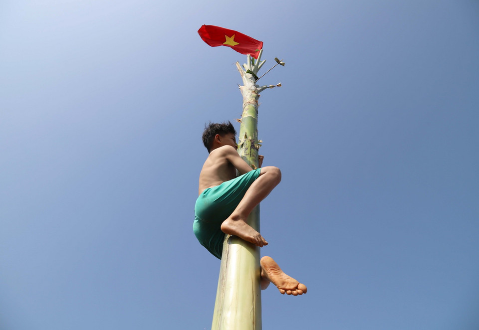 Vận động viên này đã cởi áo để tăng độ ma sát giữa cơ thể và thân chuối, quyết tâm leo lên cao hơn để giành phần thưởng. (Ảnh: Xuân Tiến/TTXVN)