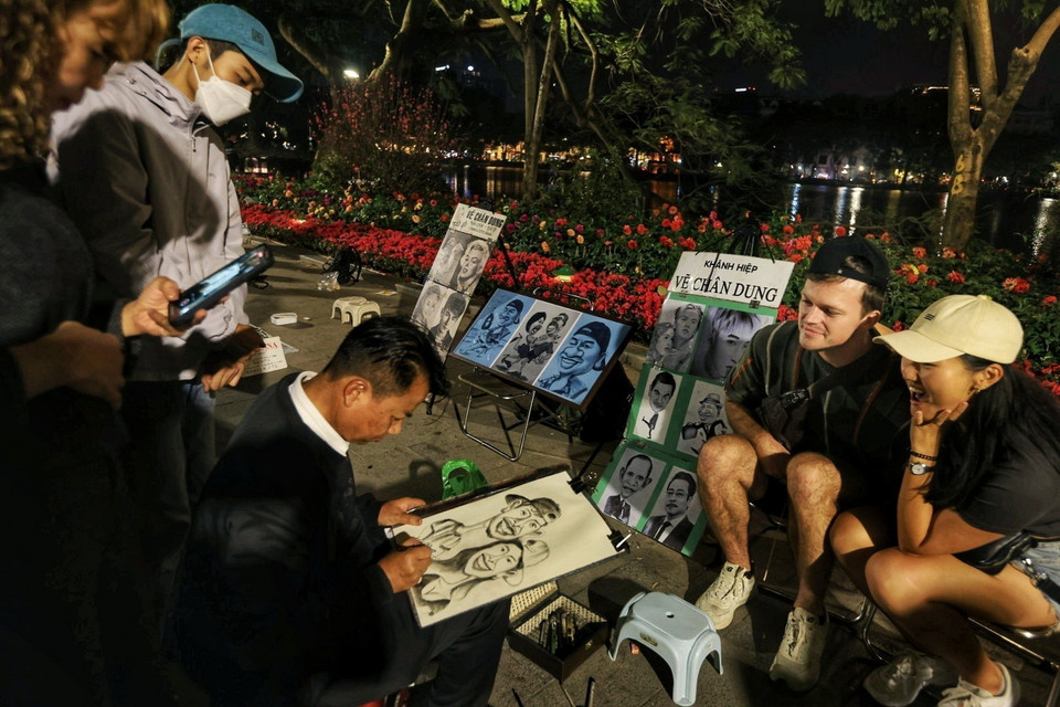 Một đôi bạn trẻ người nước ngoài thích thú khi có được bức vẽ truyền thần. (Ảnh: Tuấn Anh/TTXVN)