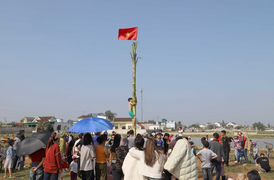 Những vận động viên tham gia thử thách leo cây chuối đang cố gắng hoàn tất lượt chơi của bản thân trong tiếng reo hò, cổ vũ sôi nổi của người dân. (Ảnh: Xuân Tiến/TTXVN)