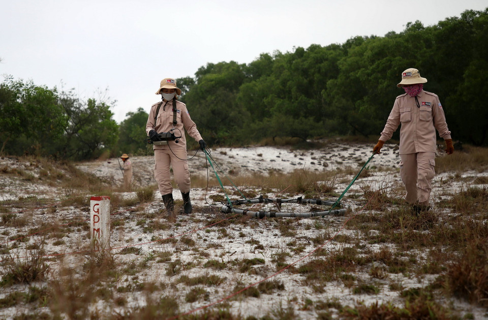 Các thành viên đội MAT 19 rà tìm các vật liệu nổ bằng máy chuyên dụng tại vùng cát huyện Hải Lăng. (Ảnh: Hồ Cầu/TTXVN)
