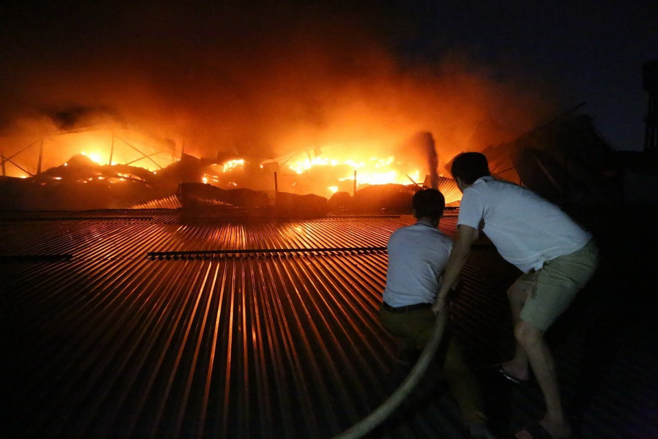 Người dân phối hợp cùng lực lượng Cảnh sát Phòng cháy chữa cháy tham gia dập lửa trong vụ cháy lớn tại khu xưởng đèn led và thiết bị chiếu sáng của Công ty Bóng đèn phích nước Rạng Đông, quận Thanh Xuân, Hà Nội. (Ảnh: Thành Đạt/TTXVN)