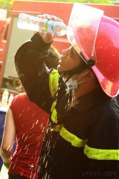 Một chiến sỹ bị lửa táp vào mặt phải dùng đến nước để tránh bỏng mắt khi tham gia dập lửa trong vụ cháy lớn tại cây xăng số 2B Trần Hưng Đạo, Hà Nội. (Ảnh: Doãn Tấn/TTXVN)