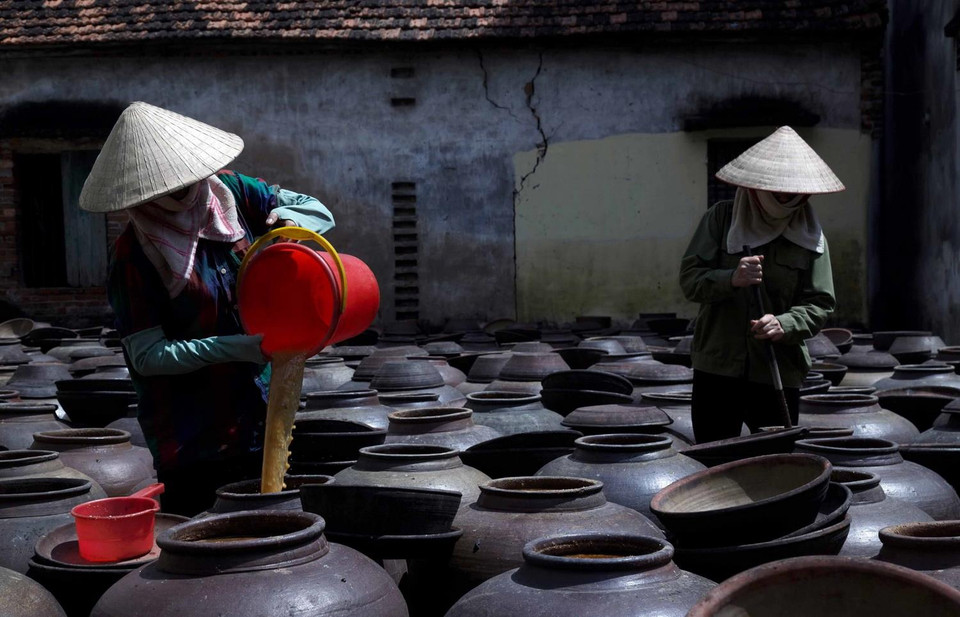 Tương được phơi nắng trong vòng ít nhất 1 tháng và luôn được theo dõi cẩn thận. Hàng ngày người thợ phải mở nắp chum khuấy đều và cho thêm nước vào tương, trời nắng thì phơi, trời mưa thì phủ kín miệng để nước mưa không lọt vào tương nếu không tương sẽ bị ủng. (Ảnh: Phạm Kiên/TTXVN)