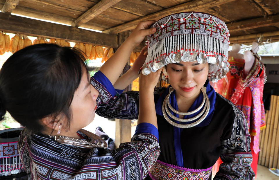 Một du khách được người dân địa phương hướng dẫn cách mặc trang phục của đồng bào Mông. (Ảnh: Tuấn Anh/TTXVN)