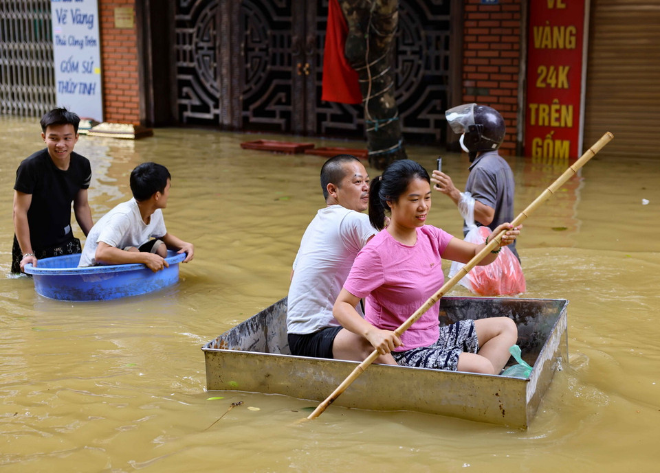 Người dân xã Bát Tràng dùng nhiều vật dụng khác nhau để có thể di chuyển như thuyền, bè trên đường bị ngập. (Ảnh: Thanh Tùng/TTXVN)