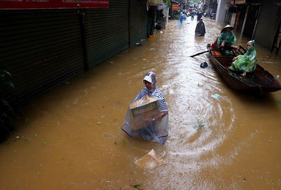 Người dân lội bì bõm trong dòng nước lũ trên phố Phúc Tân, phường Phúc Tân, quận Hoàn Kiếm (ảnh chụp lúc 14h). (Ảnh: An Đăng/TTXVN)