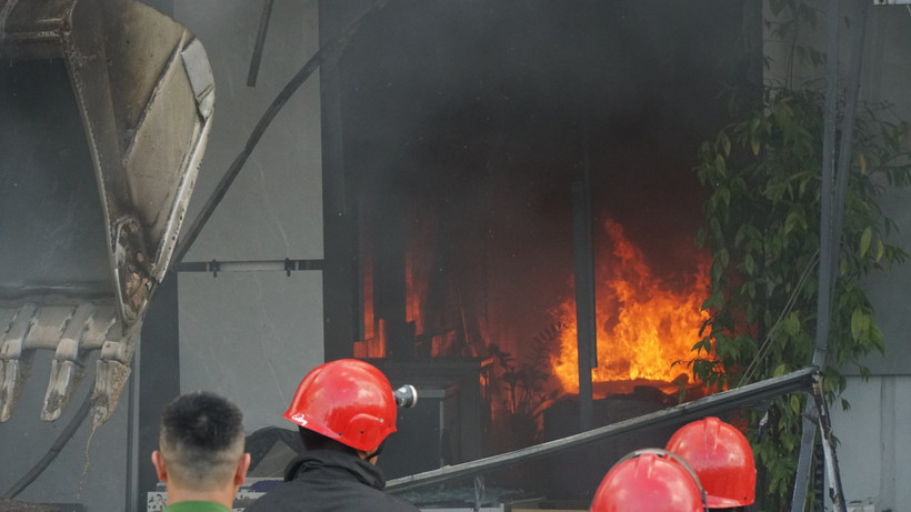 Lực lượng chức năng huy động xe cần cẩu phá mặt tiền bằng tôn của cửa hàng để phun nước vào trong. (Ảnh: Quốc Dũng/TTXVN)