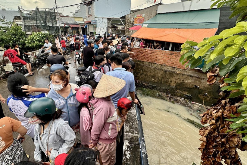 Nhiều người dân hiếu kỳ đứng xem lực lượng chức năng tìm kiếm tại đoạn suối nơi bé gái bị nước cuốn mất tích. (Ảnh: Lê Xuân/TTXVN)