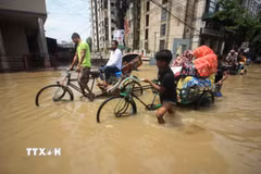 Một em nhỏ cùng những người lớn trong dòng nước lũ ở Sylhet, Bangladesh, ngày 19/5/2022. (Ảnh: AFP/TTXVN)