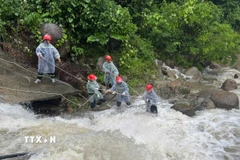 Lực lượng chức năng căng dây để trục vớt thi thể người đàn ông dưới dòng nước chảy siết. (Ảnh: TTXVN phát)