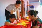 Cháu Huệ thường xuyên tới nhà chị Nhung để thêu cờ cùng các bậc cao niên. Bà Thiết và chị Nhung hướng dẫn bé Huệ đi đường kim sao cho chính xác và đẹp nhất. (Ảnh: Hoài Nam/Vietnam+)
