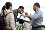 Anh Đặng Vũ Tuấn Sơn (phải) hướng dẫn các bạn trẻ quan sát bầu trời qua kính thiên văn. (Ảnh: Doãn Đức/Vietnam+)