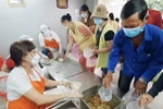 Các thành viên tại Bếp yêu thương chia từng phần cháo chay nóng hổi đến cho người dân tại Bệnh viện Chợ Rẫy. (Ảnh: Thu Hương/TTXVN)