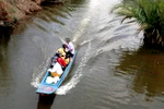 Các em học sinh ở Tiểu khu 34, ấp Cán Gáo đến trường bằng thuyền. (Ảnh: Lê Sen/TTXVN)