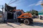 Lực lượng chức năng điều xe múc tới đập tường nhà, dọn dẹp xà bần để tiếp cận vị trí ba người bị mắc kẹt trong nhà. (Ảnh: Nguyễn Thành/TTXVN) 