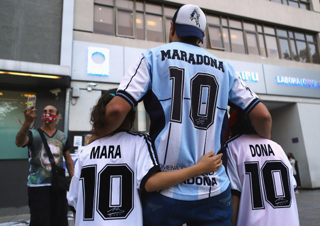 Cổ động viên Walter Rotundo chụp ảnh cùng 2 con gái song sinh Mara và Dona bên ngoài bệnh viện nơi Diego Maradona thực hiện ca phẫu thuật não ở Buenos Aires. (Ảnh: Reuters) Tinh thần "cháy hết mình" của Maradona còn mãi trong lòng người hâm mộ ảnh 1